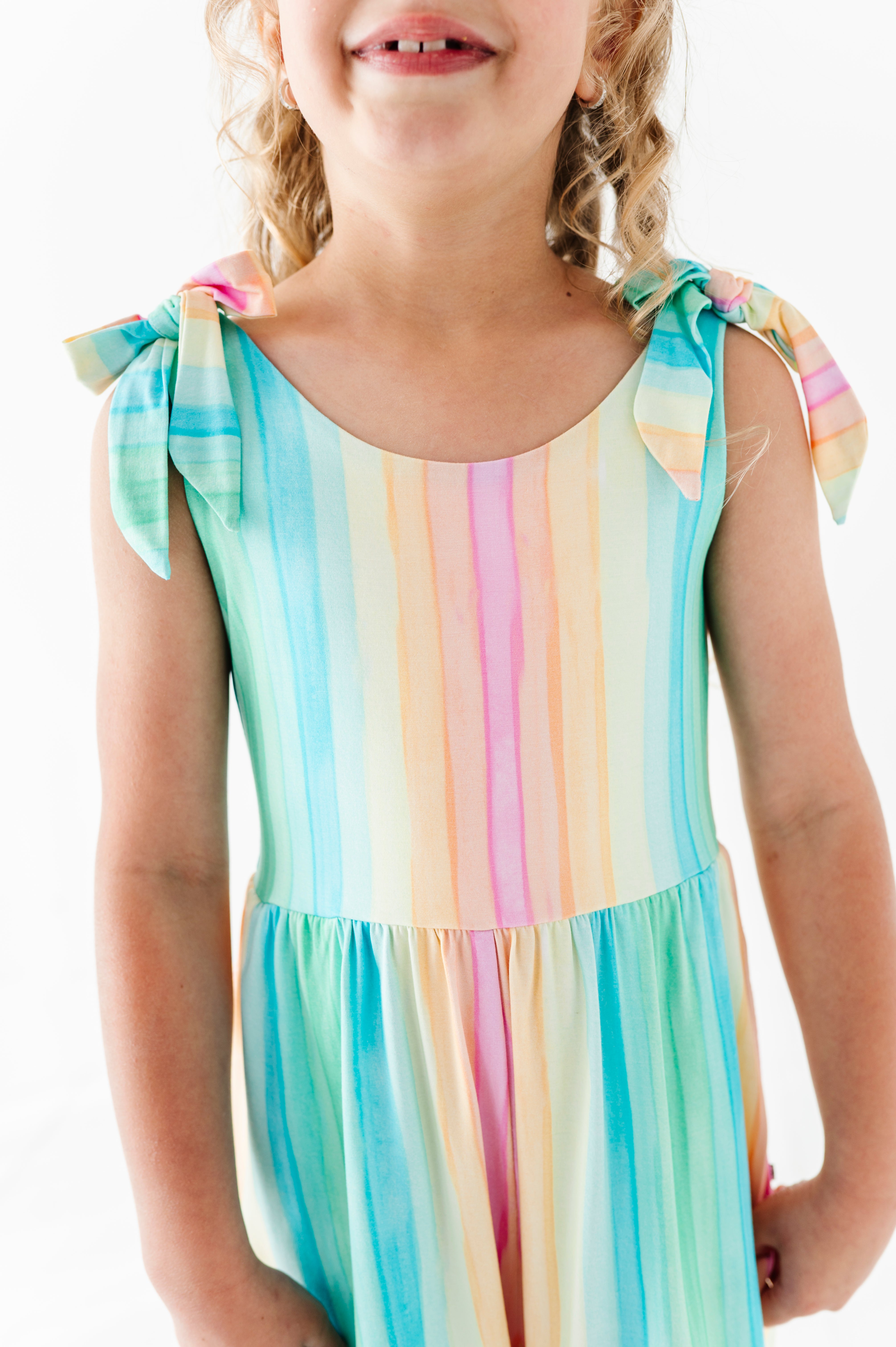 Child wearing a colorful striped romper with bow straps on a white background
