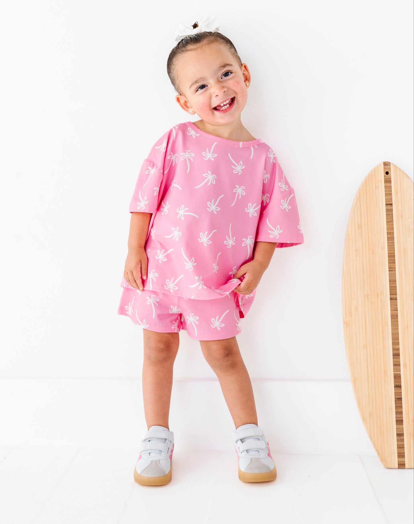 Child wearing a pink outfit with white palm tree patterns on a white background