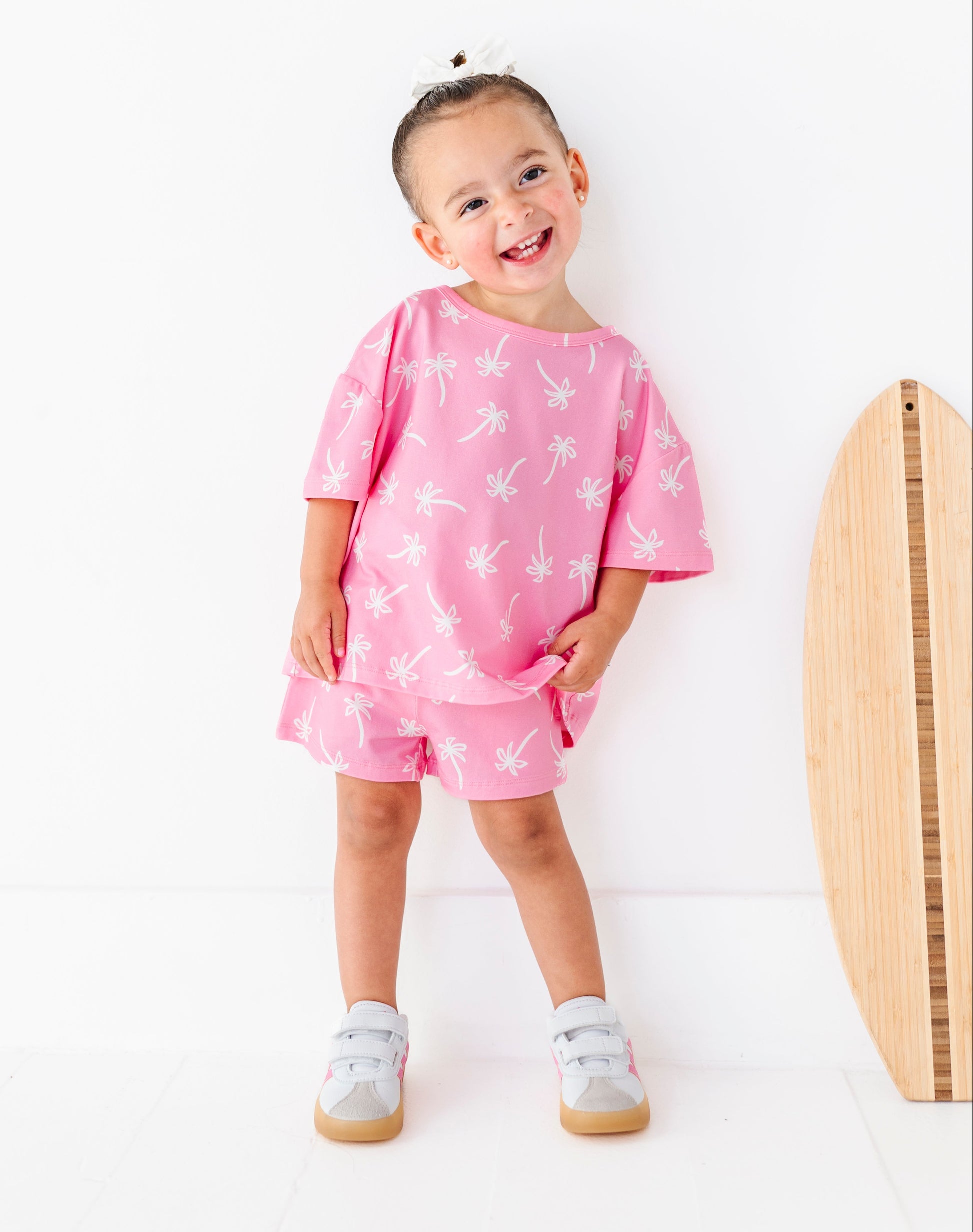 Child wearing a pink outfit with white palm tree patterns on a white background