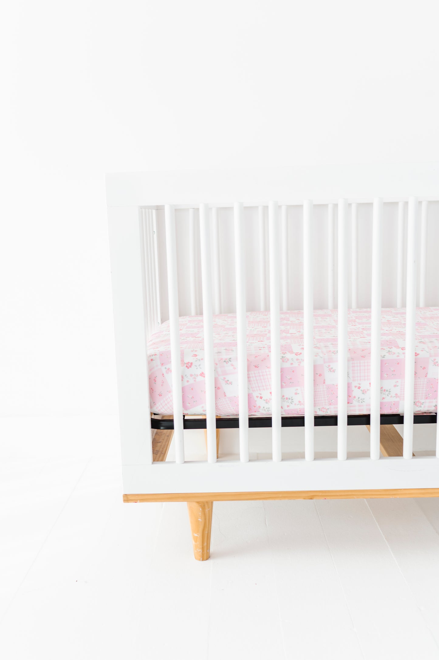 White crib with a pink bamboo crib sheet on a white background