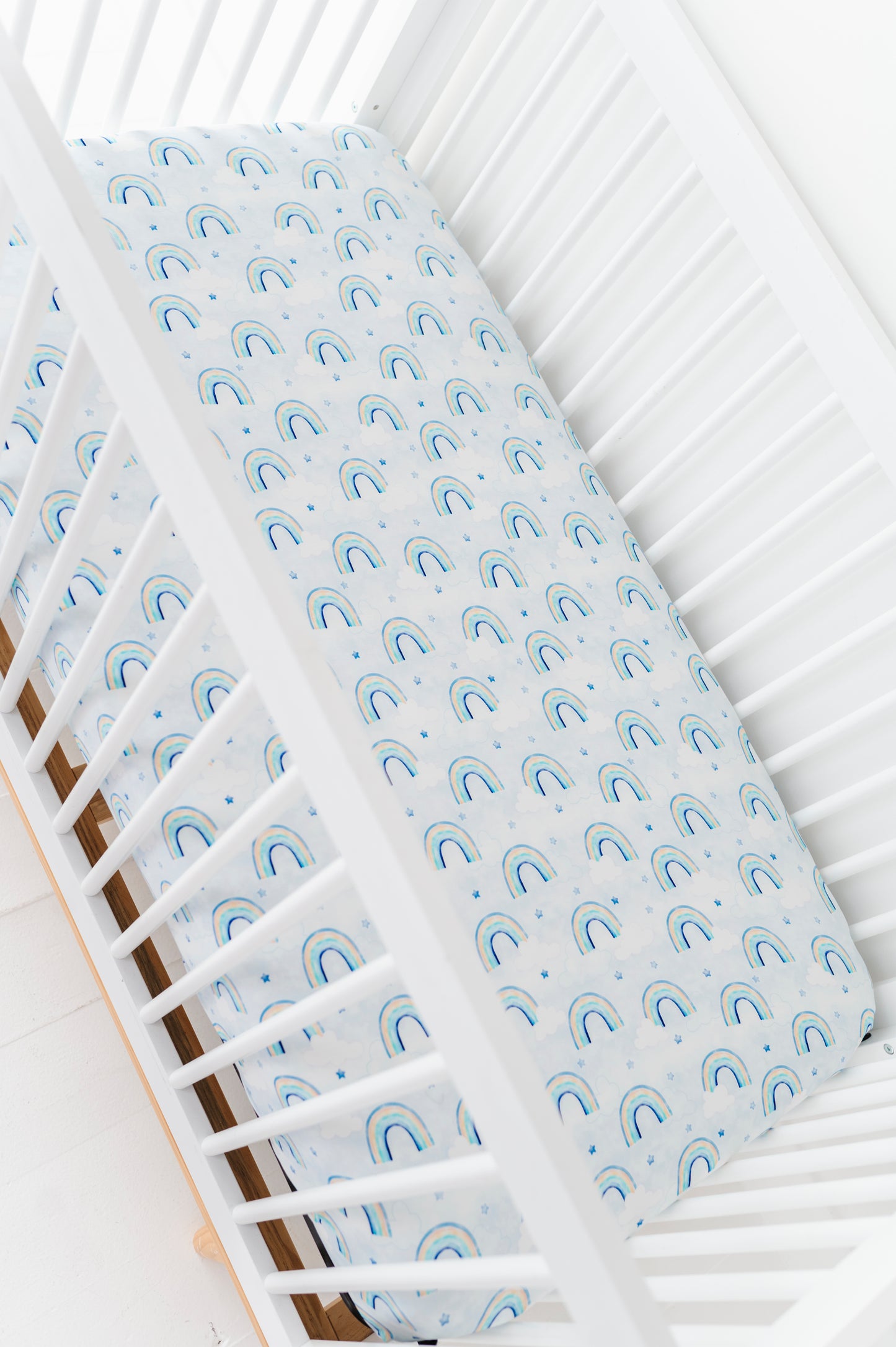 Bamboo crib sheet with blue watercolor rainbow pattern on a white crib