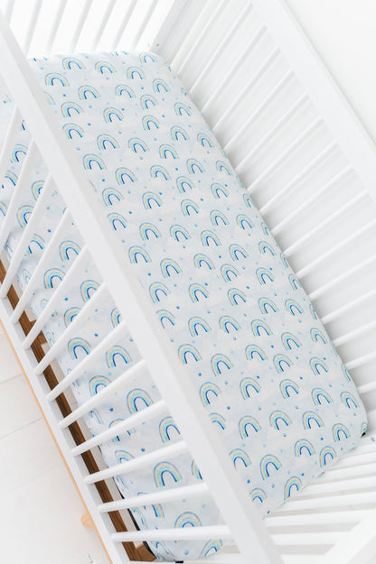 Bamboo crib sheet with blue watercolor rainbow pattern on a white crib