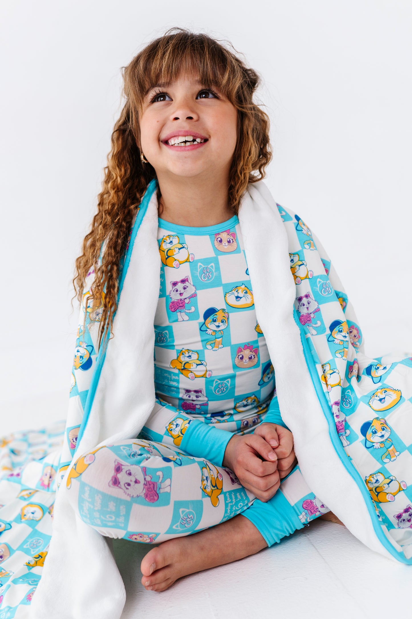 Child wearing a colorful 44 Cats pajama set and wrapped in a matching plush bamboo blanket 