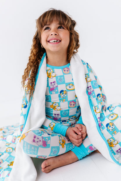 Child wearing a colorful 44 Cats pajama set and wrapped in a matching plush bamboo blanket 