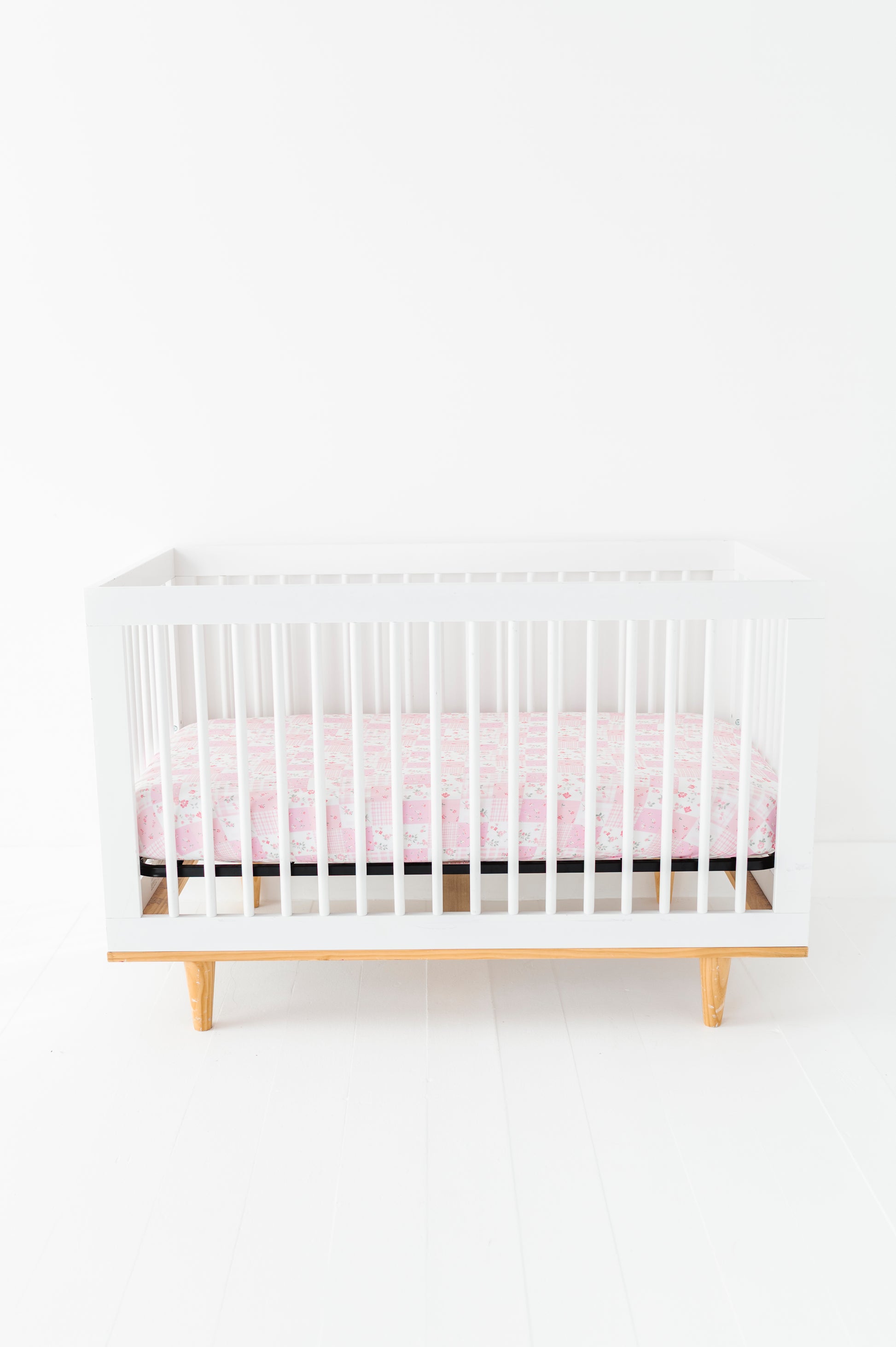 White crib with a pink bamboo crib sheet on a white background