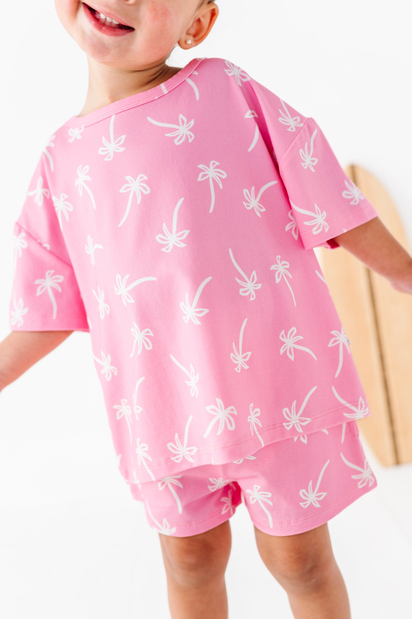 Child wearing a pink outfit with white palm tree patterns on a white background