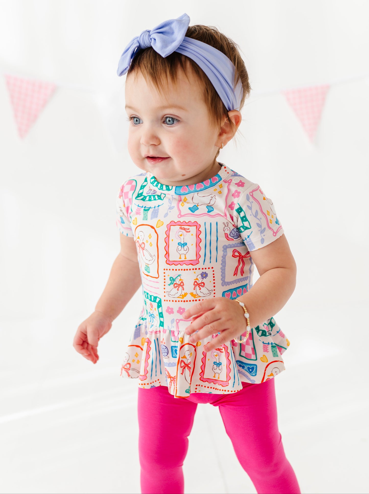 Baby wearing a colorful top and pink leggings with a white background