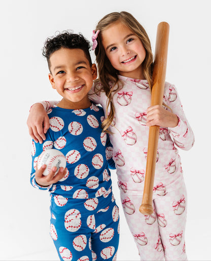Two children in bamboo pajamas with sports-themed patterns, one holding a baseball and the other a bat.