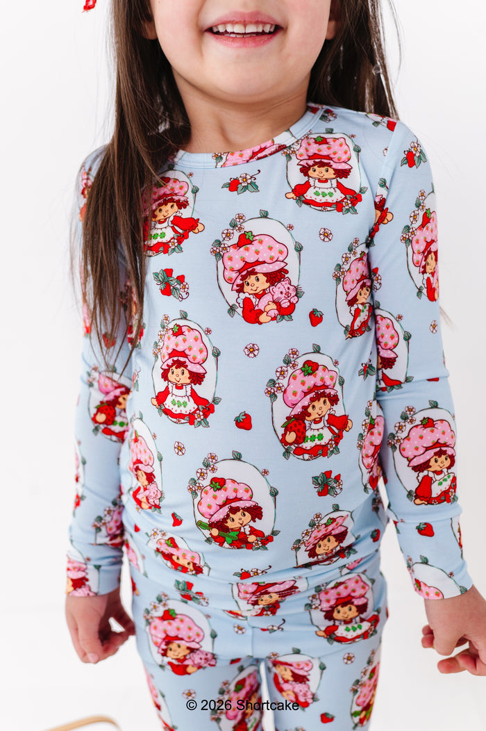 Child wearing a Strawberry Shortcake™ bamboo pajama set with a light blue background