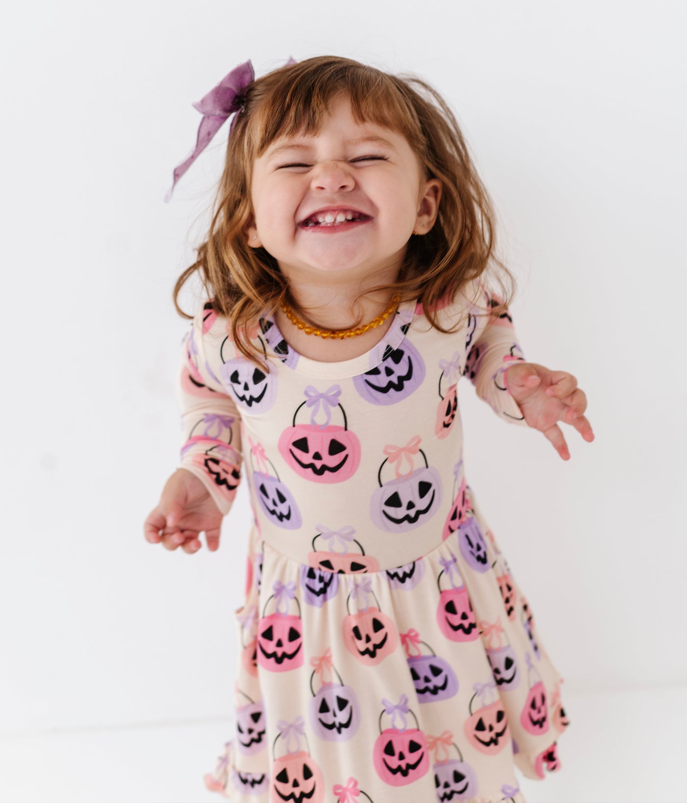 Child wearing a Halloween-themed dress with pumpkins, ghosts, and ghosts on a white background