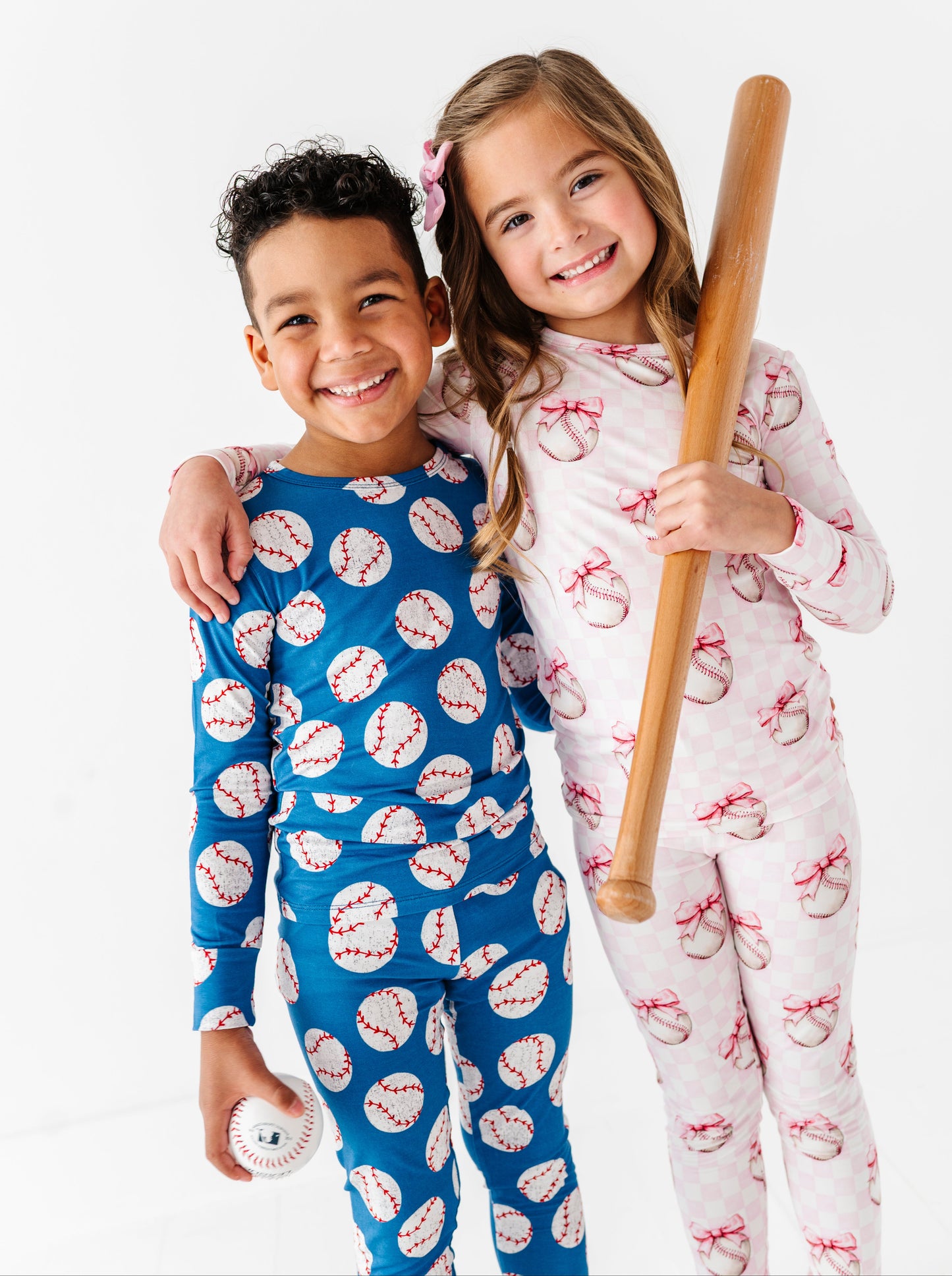 Siblings wearing bamboo pajamas with sports-themed prints, one holding a baseball bat.