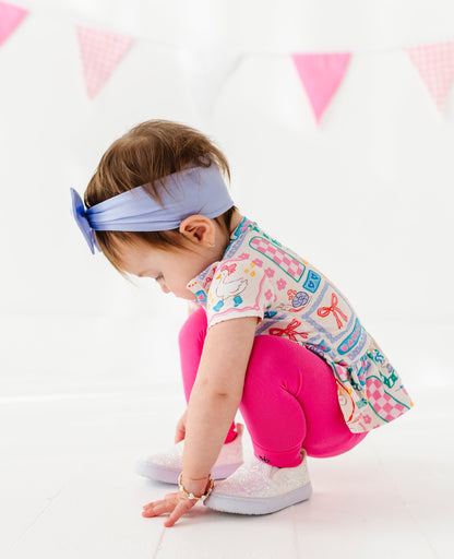 Child wearing a colorful bamboo/cotton peplum top and pink leggings with a white background and pink flags.