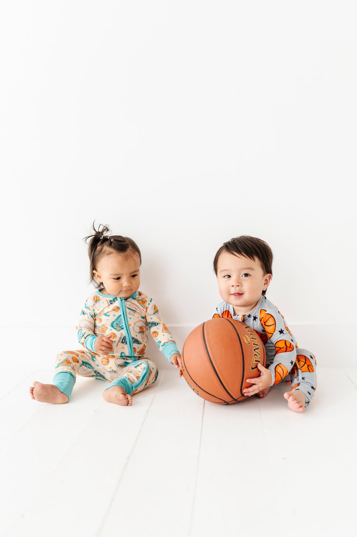 Two children in matching bamboo sports zip rompers with a basketball on a white background