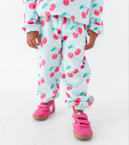 A child wearing a matching light blue cherry print fleece tracksuit with pink sneakers, shown from the neck down against a white studio background.