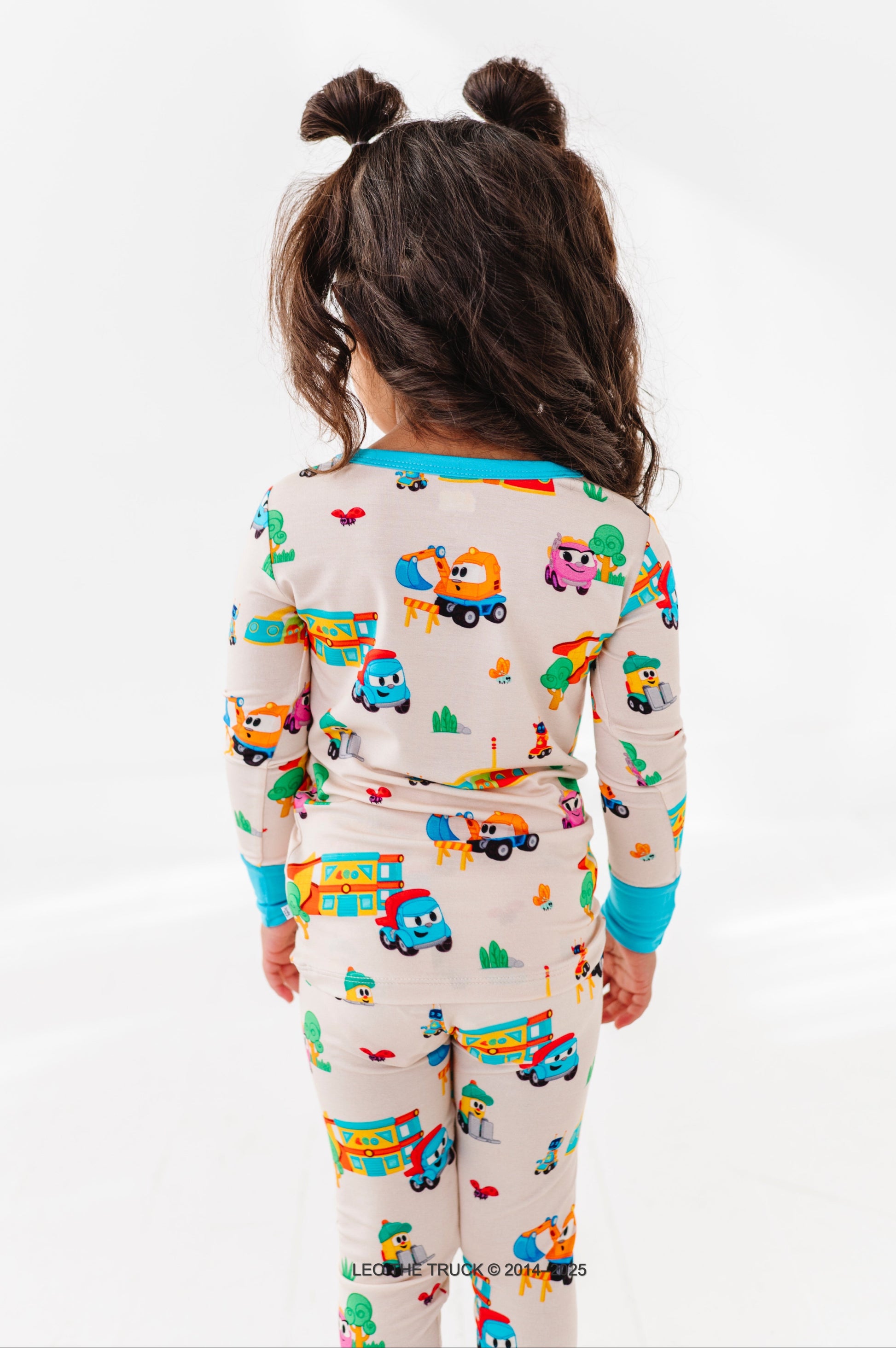 Little girl wearing colorful Leo the Truck bamboo pajamas on a white background