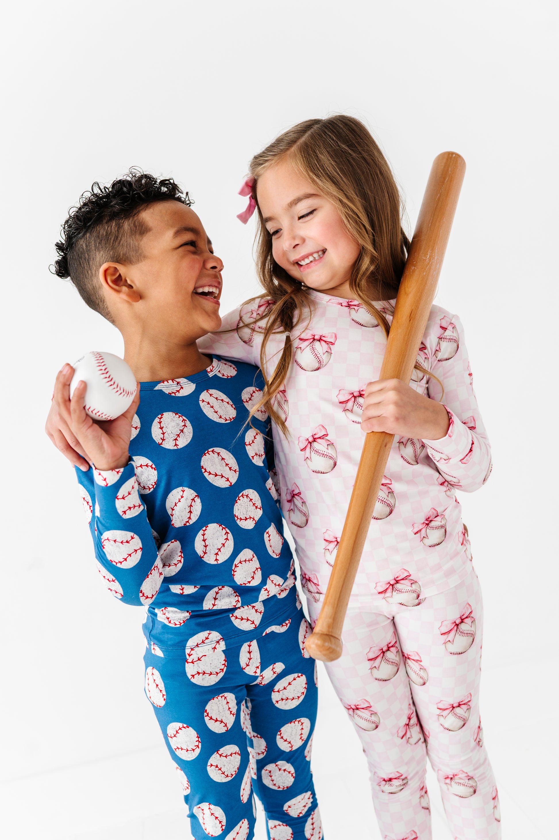Two children in bamboo pajamas with sports-themed patterns, one holding a baseball and the other a bat.