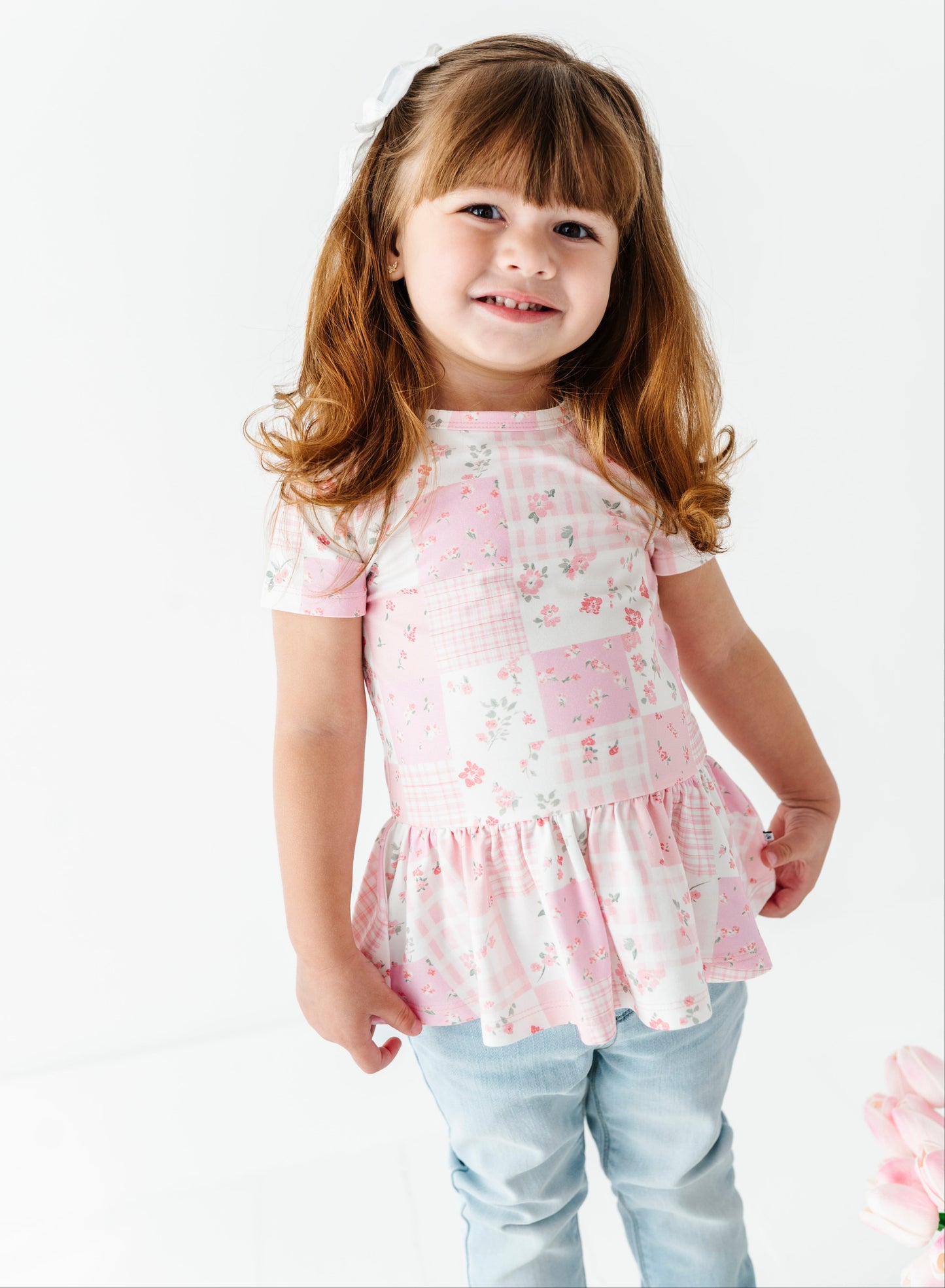 Young girl wearing a pink floral bamboo-cotton peplum top with a white background