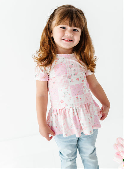 Young girl wearing a pink floral bamboo-cotton peplum top with a white background