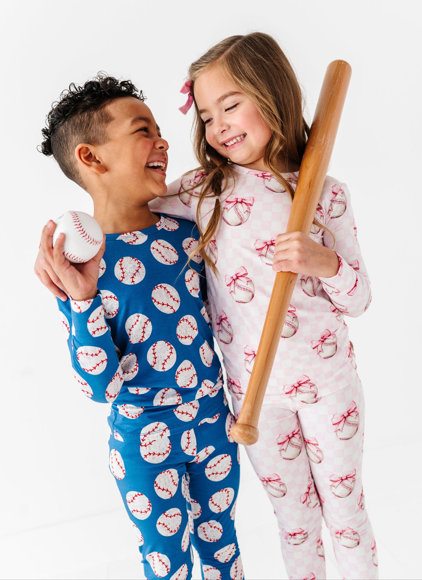 Two children in bamboo pajamas with baseball-themed patterns, one holding a baseball and the other a bat.