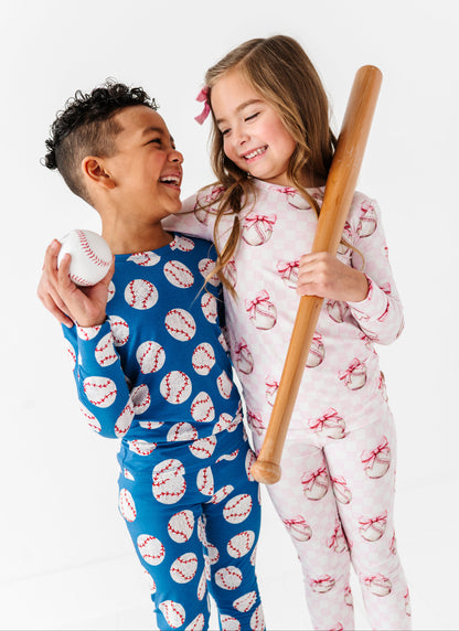 Two children in bamboo pajamas with baseball-themed patterns, one holding a baseball and the other a bat.