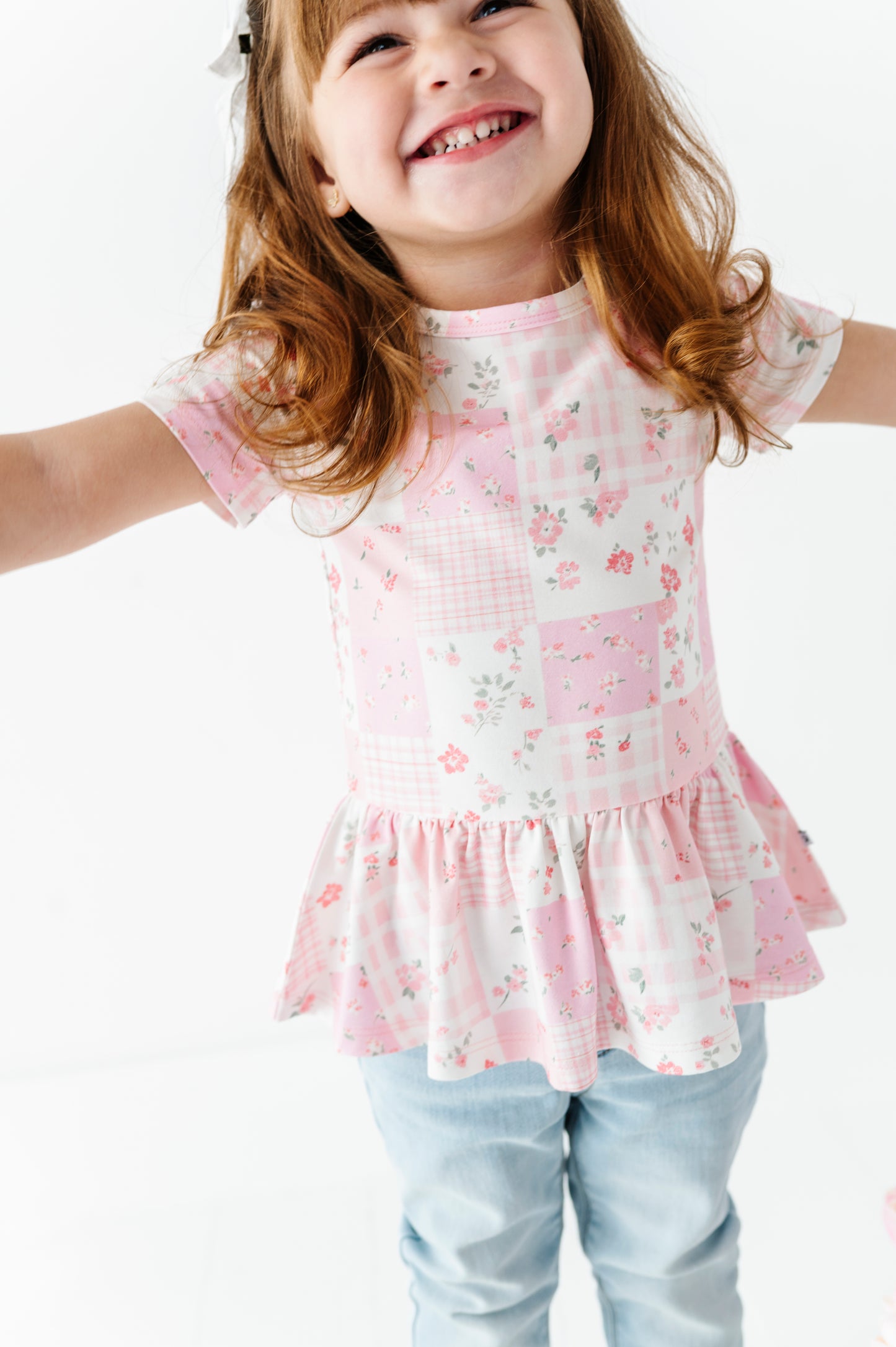 Child wearing a pink floral bamboo-cotton peplum blouse with ruffled details on a white background