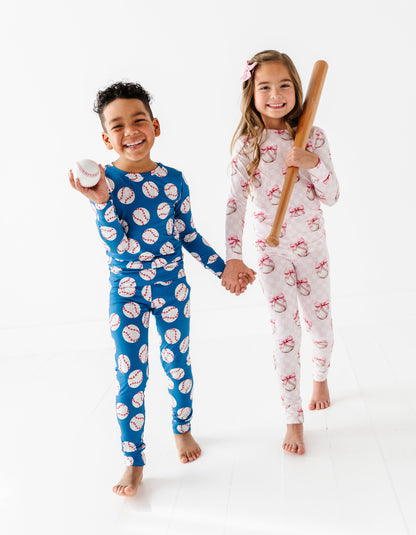 Brother and sister wearing patterned bamboo pajamas holding a baseball and bat on a white background