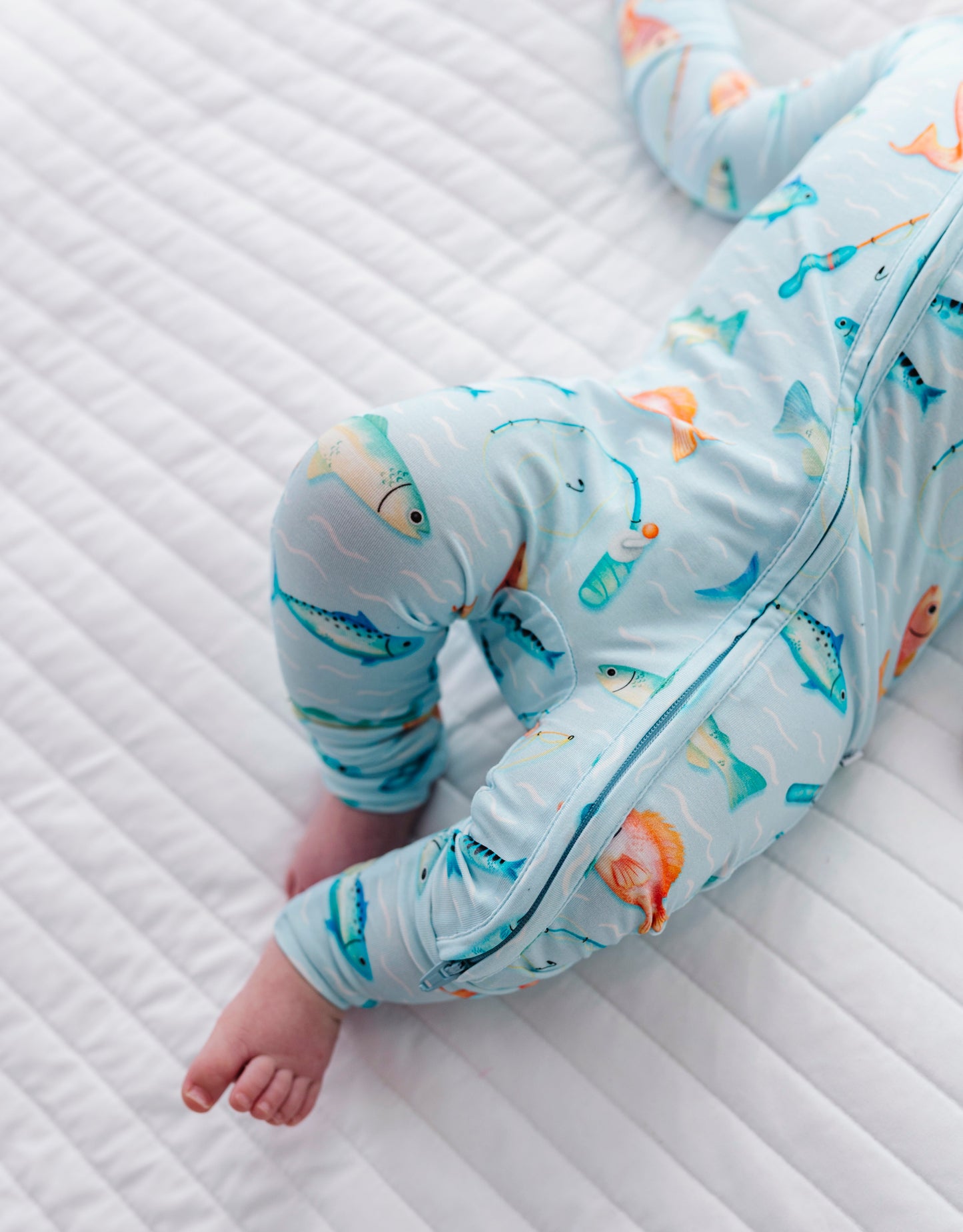 Baby in a colorful fish themed romper lying on a textured white surface