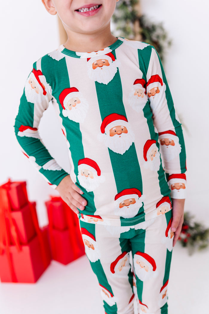 A close-up, detail photo of a green and beige stripe bamboo pajama set with Santa faces all over it. The pajamas are a ribbed bamboo material and fitted to meet CPSC standards