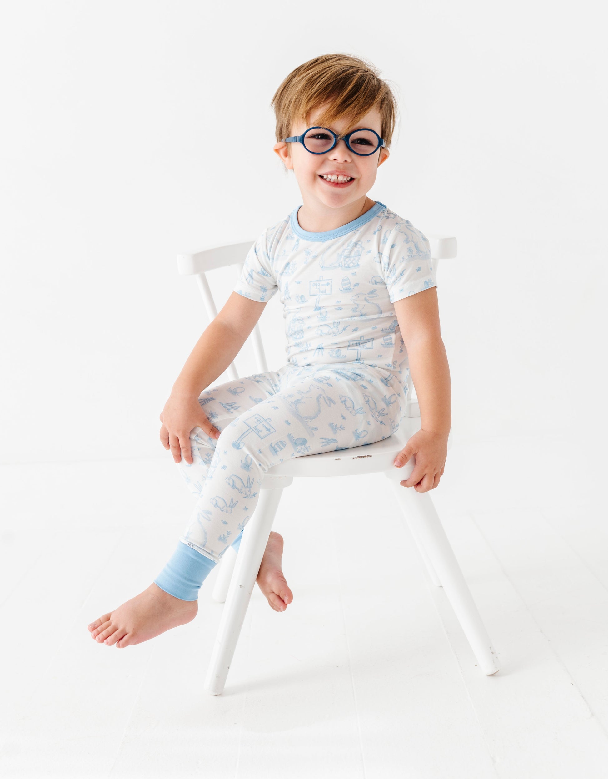 Child wearing glasses and a light-colored bamboo Easter pajama set sitting on a chair against a white background