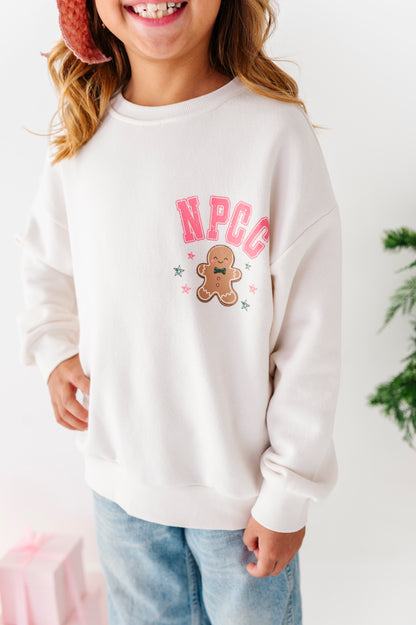 An up-close photo of a young girl wearing a bamboo crewneck. The crewneck says "NPCC" above a gingerbread cookie. 