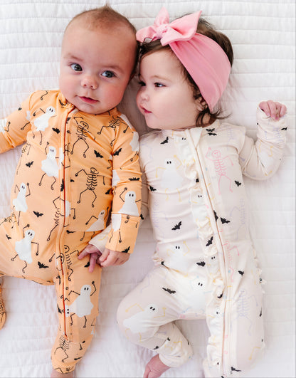 Two babies wearing Halloween-themed onesies on a white blanket.