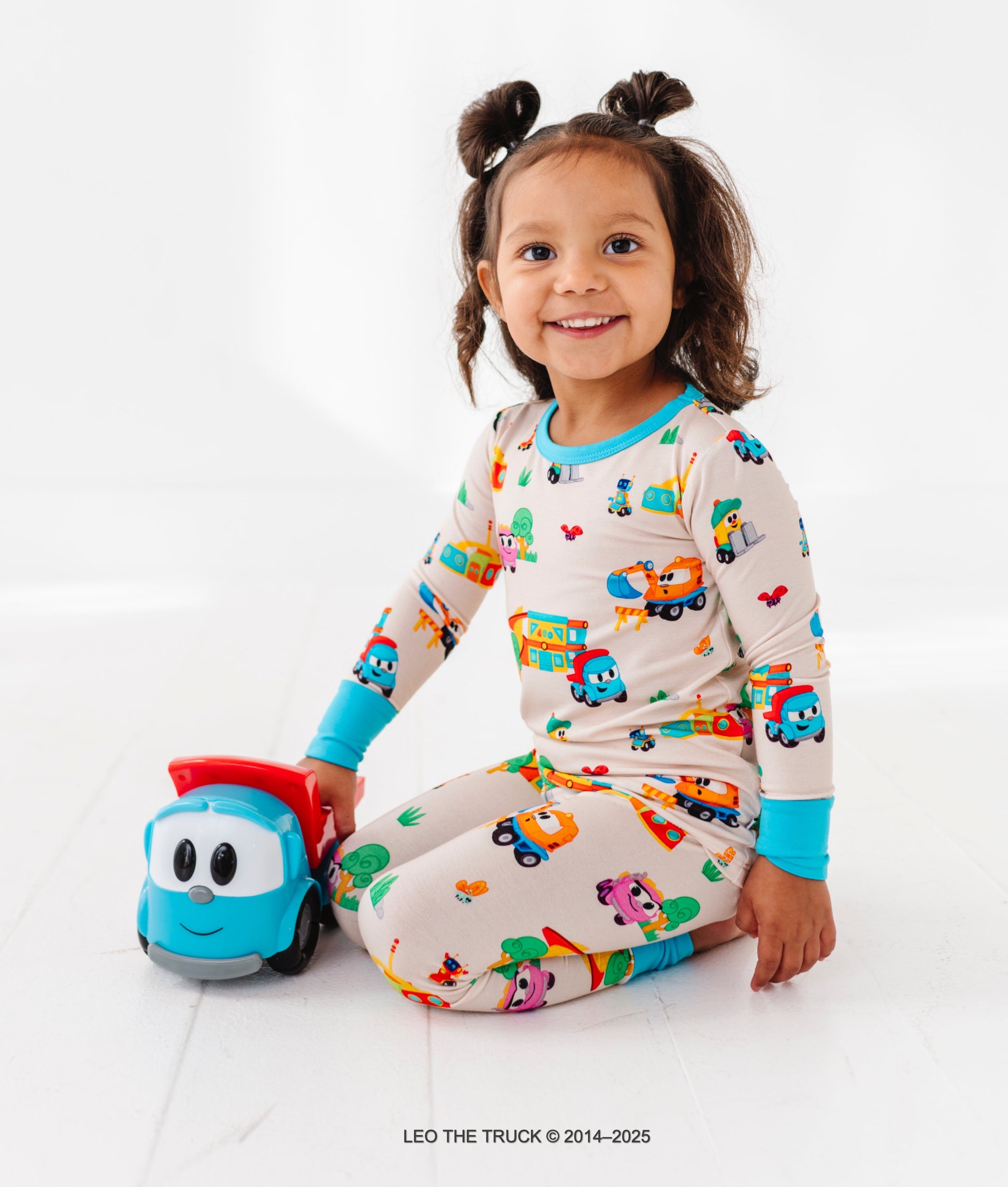 Child wearing pajamas with Leo the Truck pattern holding a toy Leo car on a white background