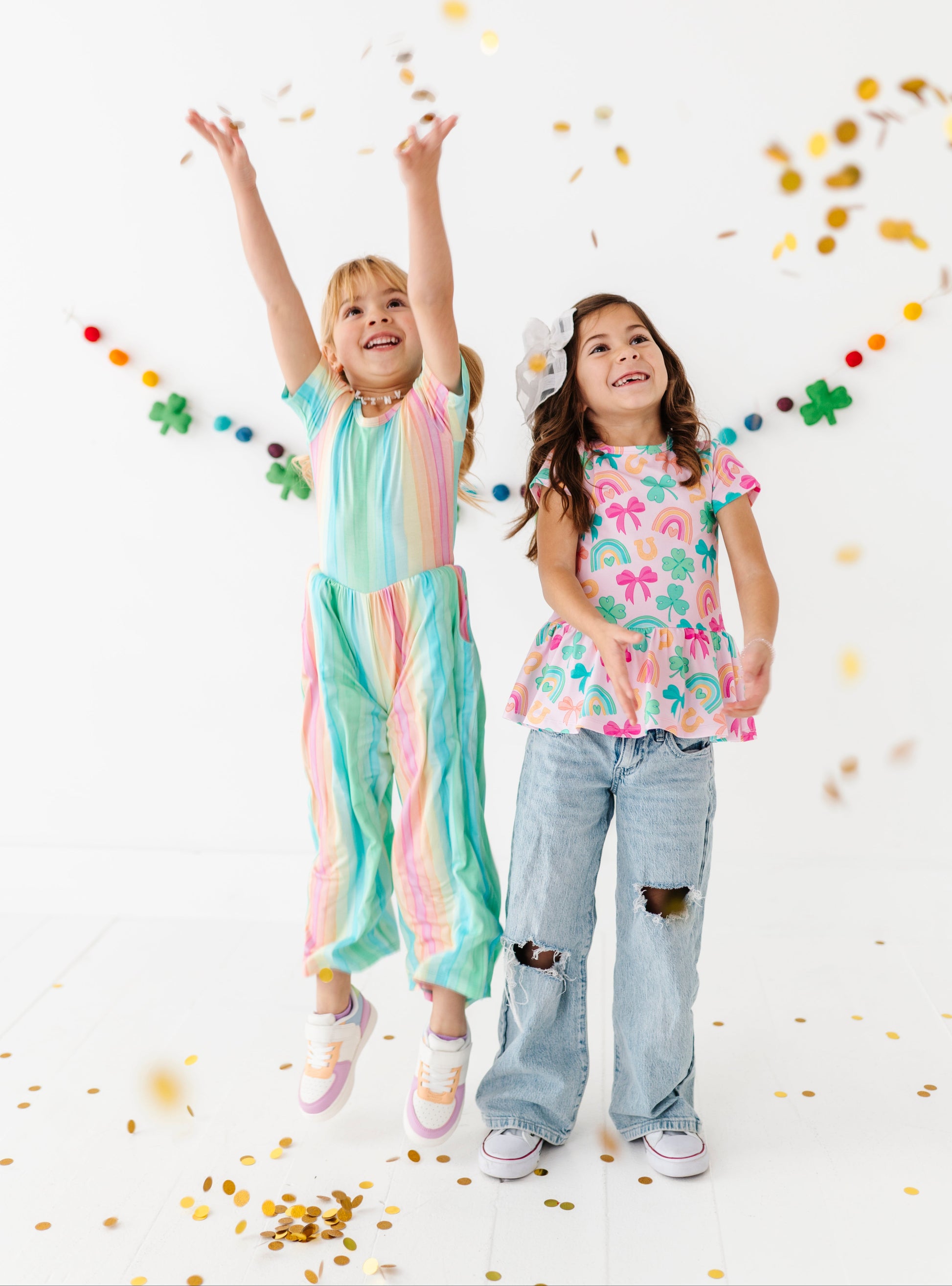 Two children in colorful St. Patrick's Day bamboo outfits standing on a white background with confetti.