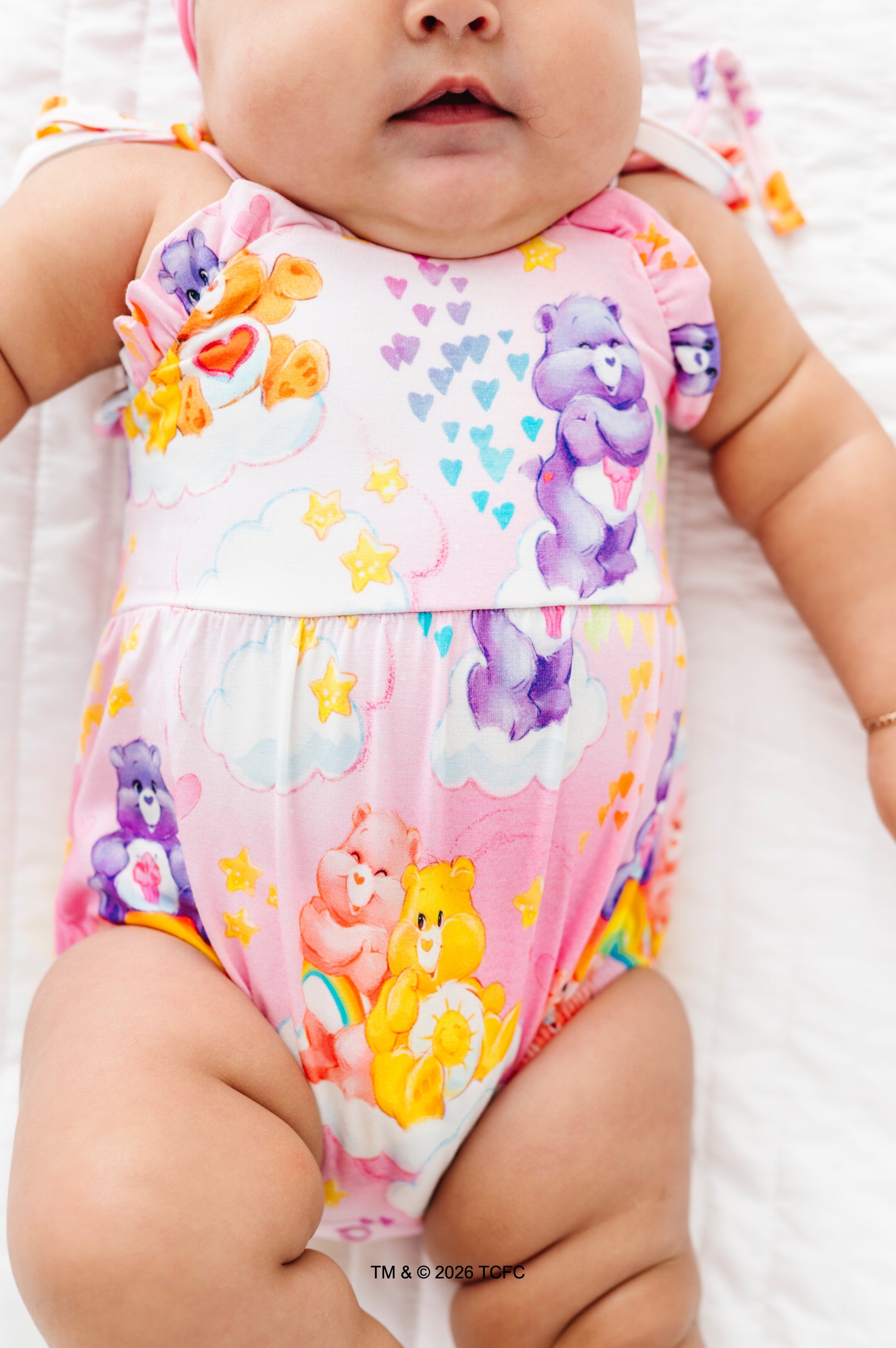 Baby wearing a colorful Care Bears™ bubble romper on a white background