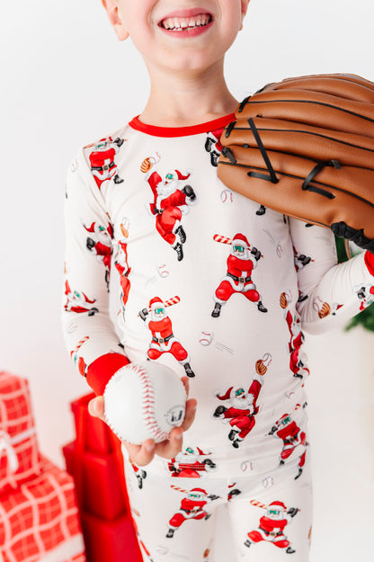 A close-up detail shot of a baseball Christmas print. A young boy is wearing the baseball Christmas pajamas and holding a baseball and leather glove. 