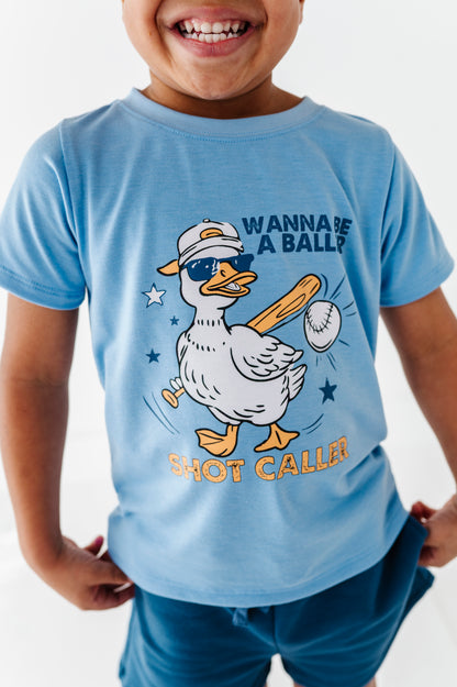 Little boy wearing a light blue baseball-themed t-shirt with a cartoon duck graphic and text.