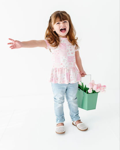 Child holding a basket of flowers wearing a bamboo-cotton peplum top on a white background