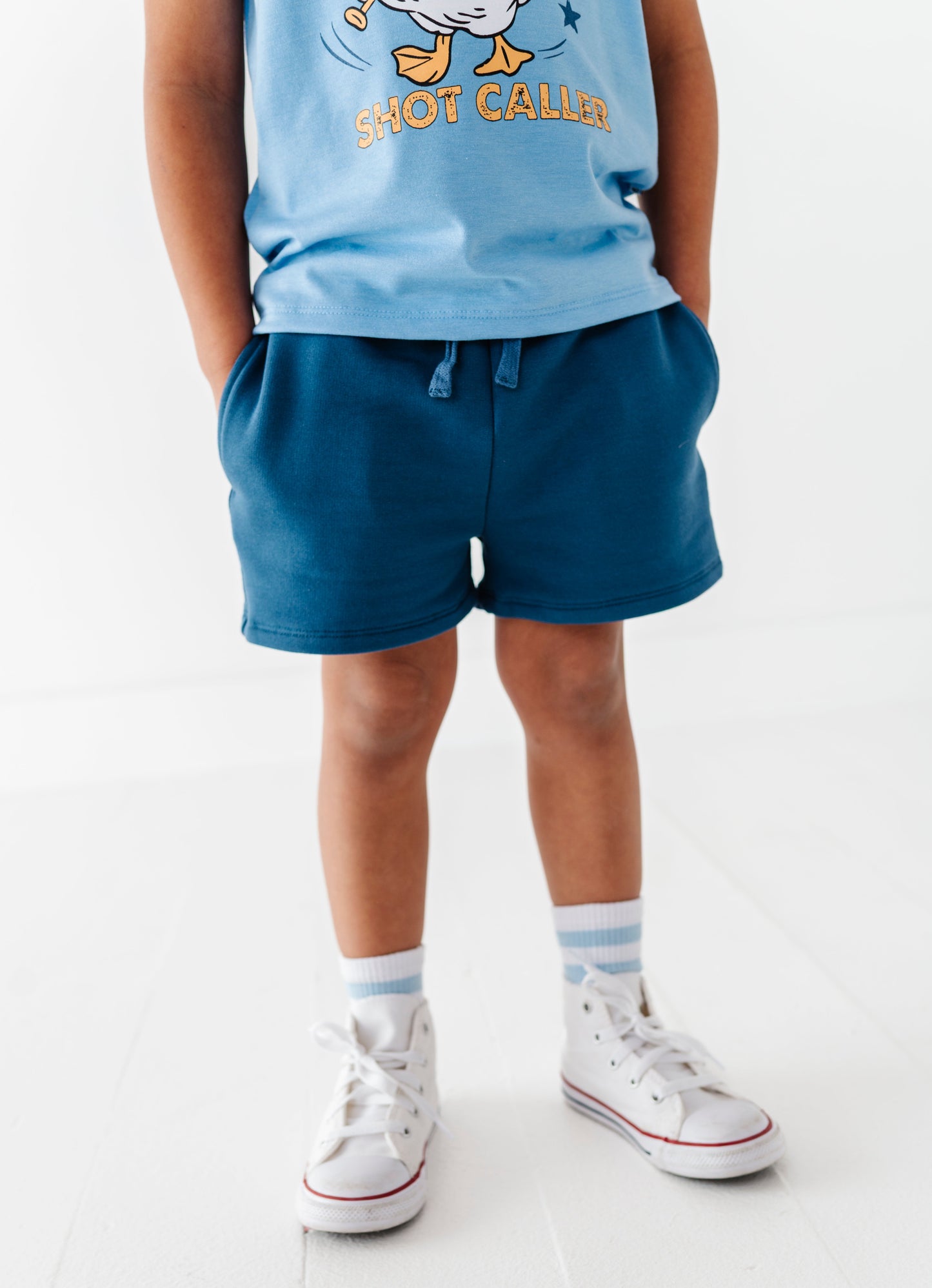 Child wearing a blue baseball shirt and navy bamboo cotton shorts on a white background