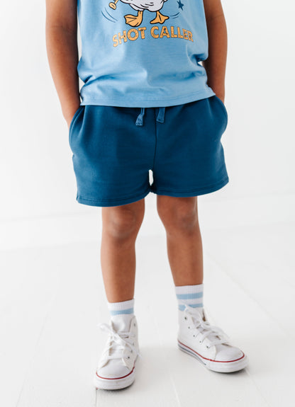 Child wearing a blue baseball shirt and navy bamboo cotton shorts on a white background