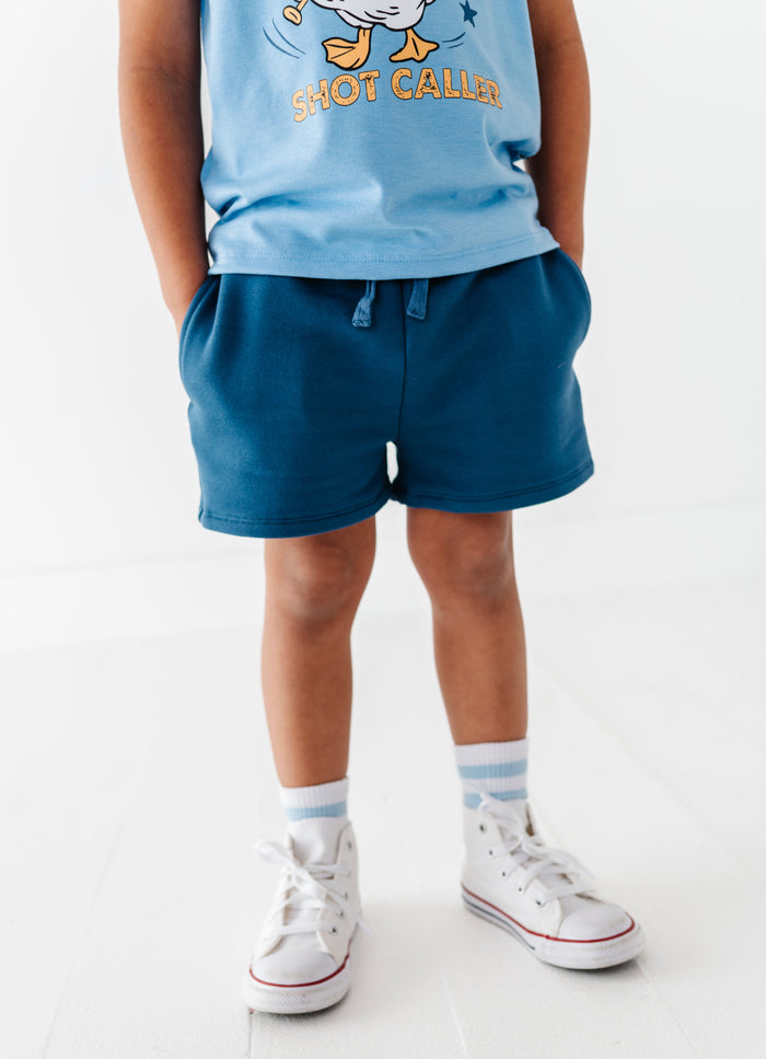 Child wearing a blue baseball shirt and navy bamboo cotton shorts on a white background