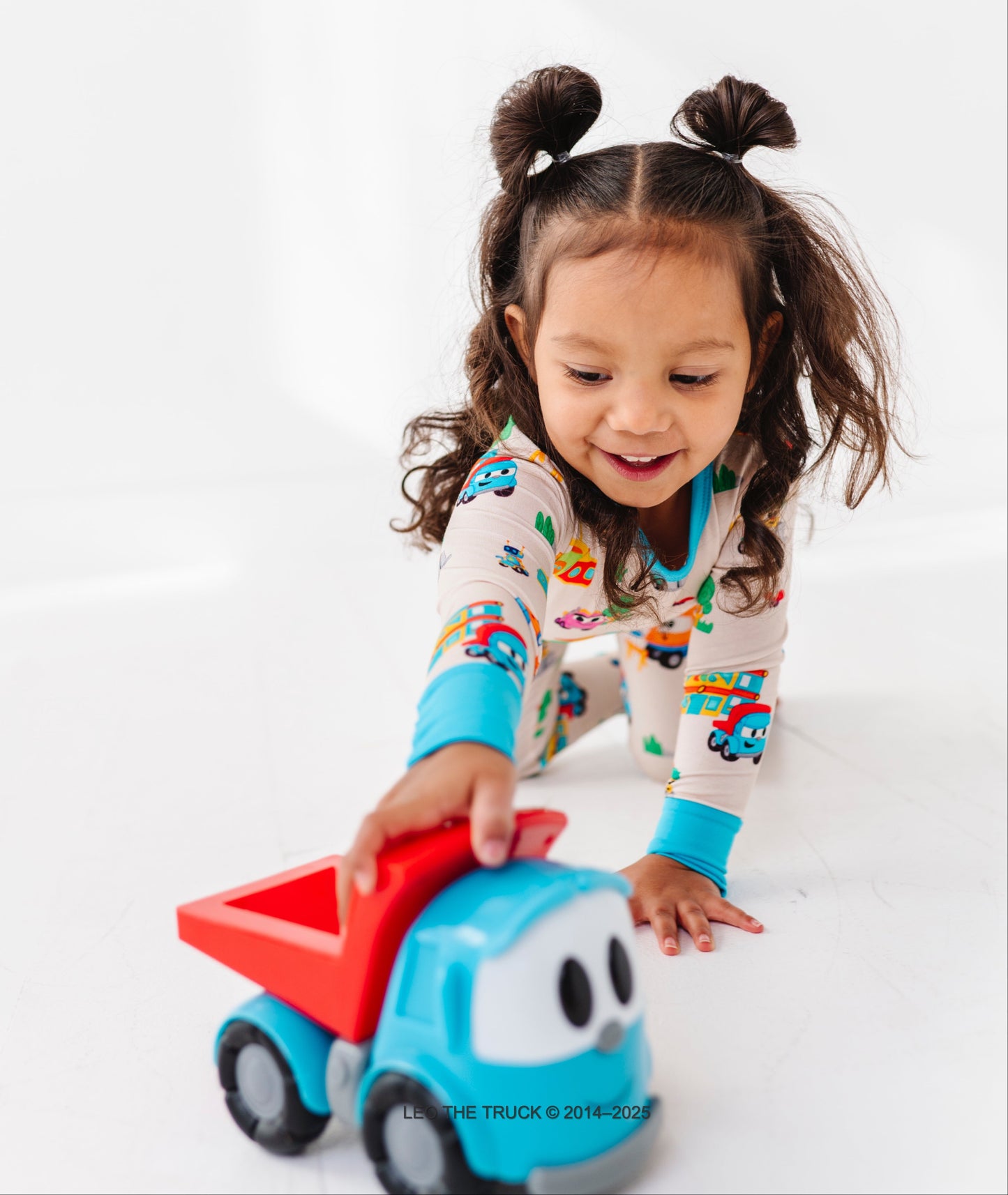 Little girl playing with a Leo the Truck toy against a white background 