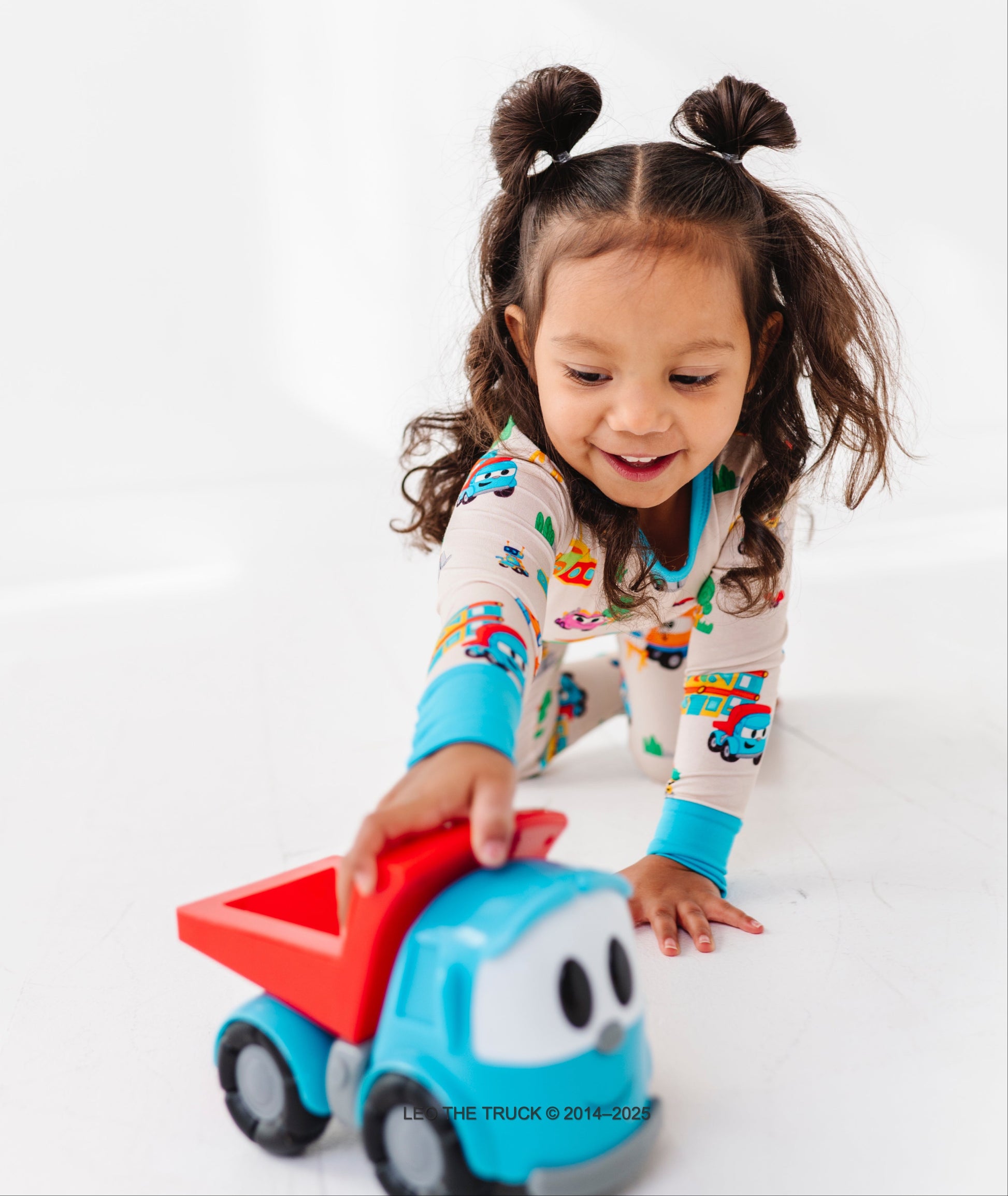 Little girl playing with a Leo the Truck toy against a white background 