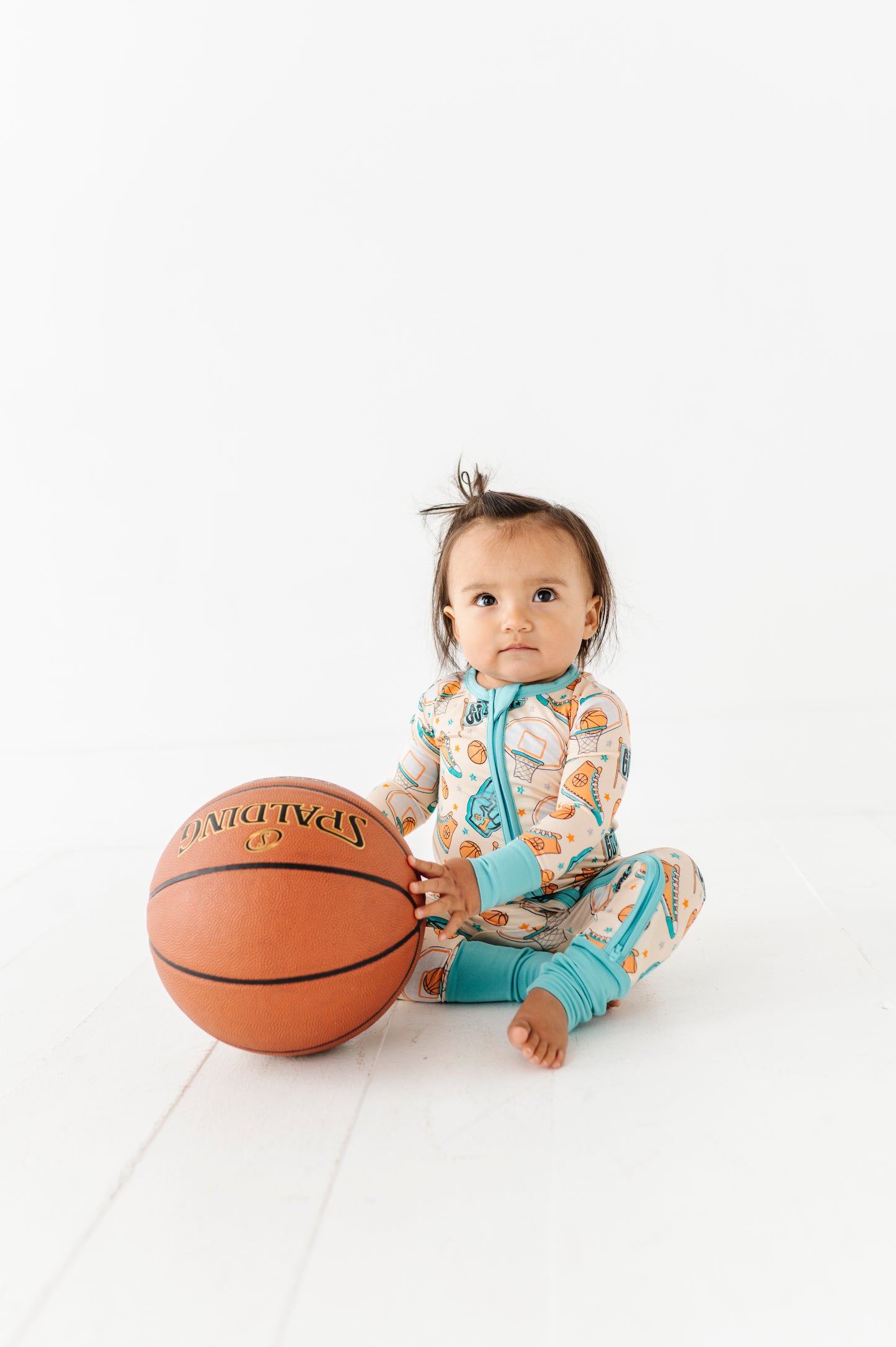 Baby wearing a basketball themed convertible romper and holding a basketball on a white background