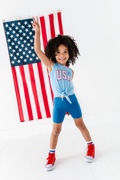 Child wearing a 'USA' tank top with an American flag in the background