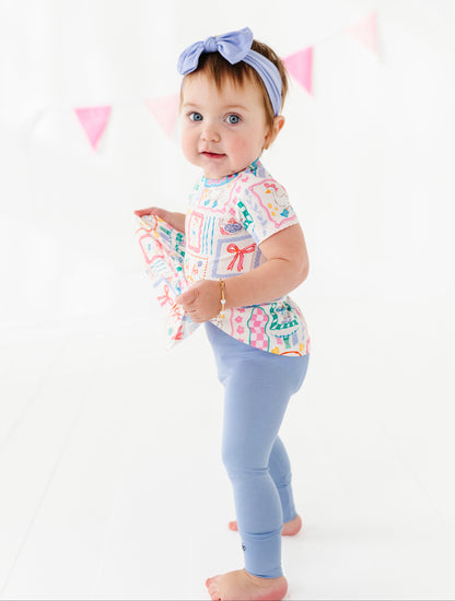 Baby wearing a colorful bamboo/cotton blend shirt and light blue leggings with a white background