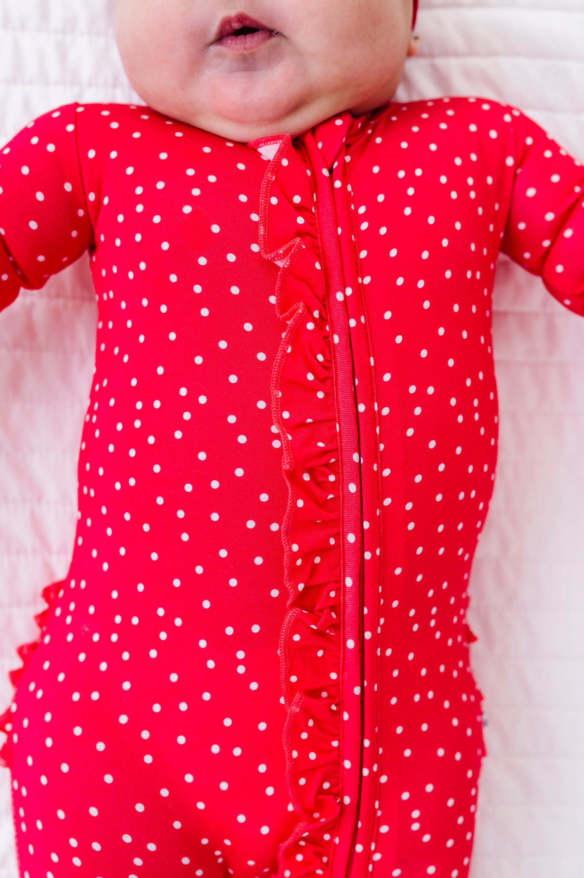 Baby wearing a red polka dot romper on a white background