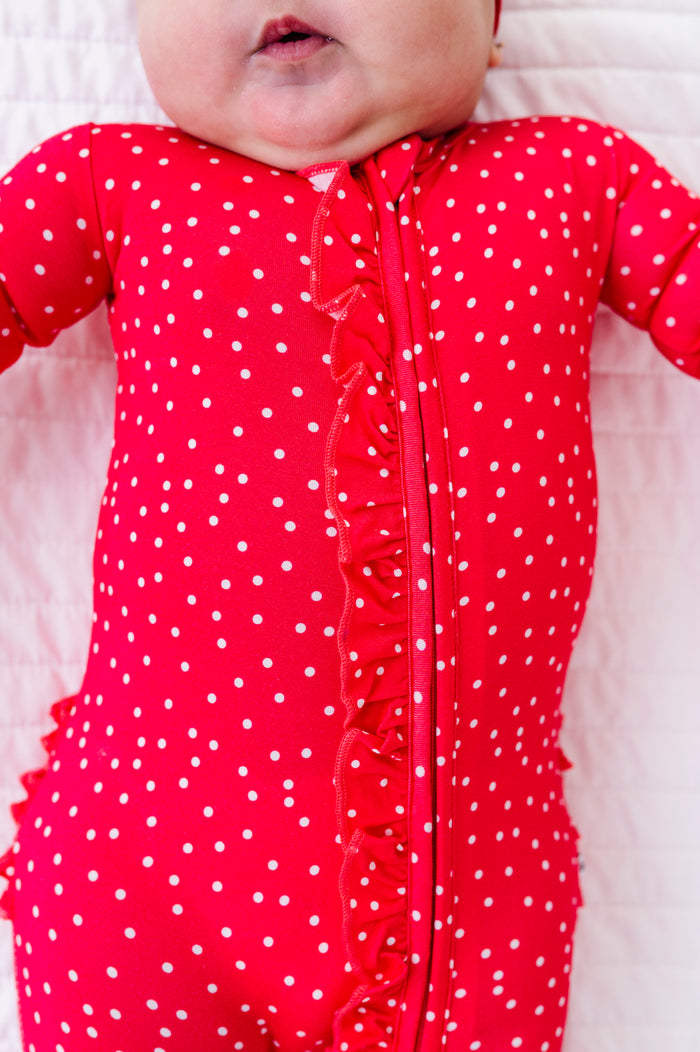 Baby wearing a red polka dot romper on a white background