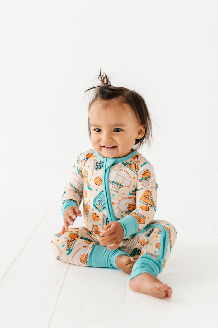 Child wearing a sports themed bamboo onesie with a zipper on a white background
