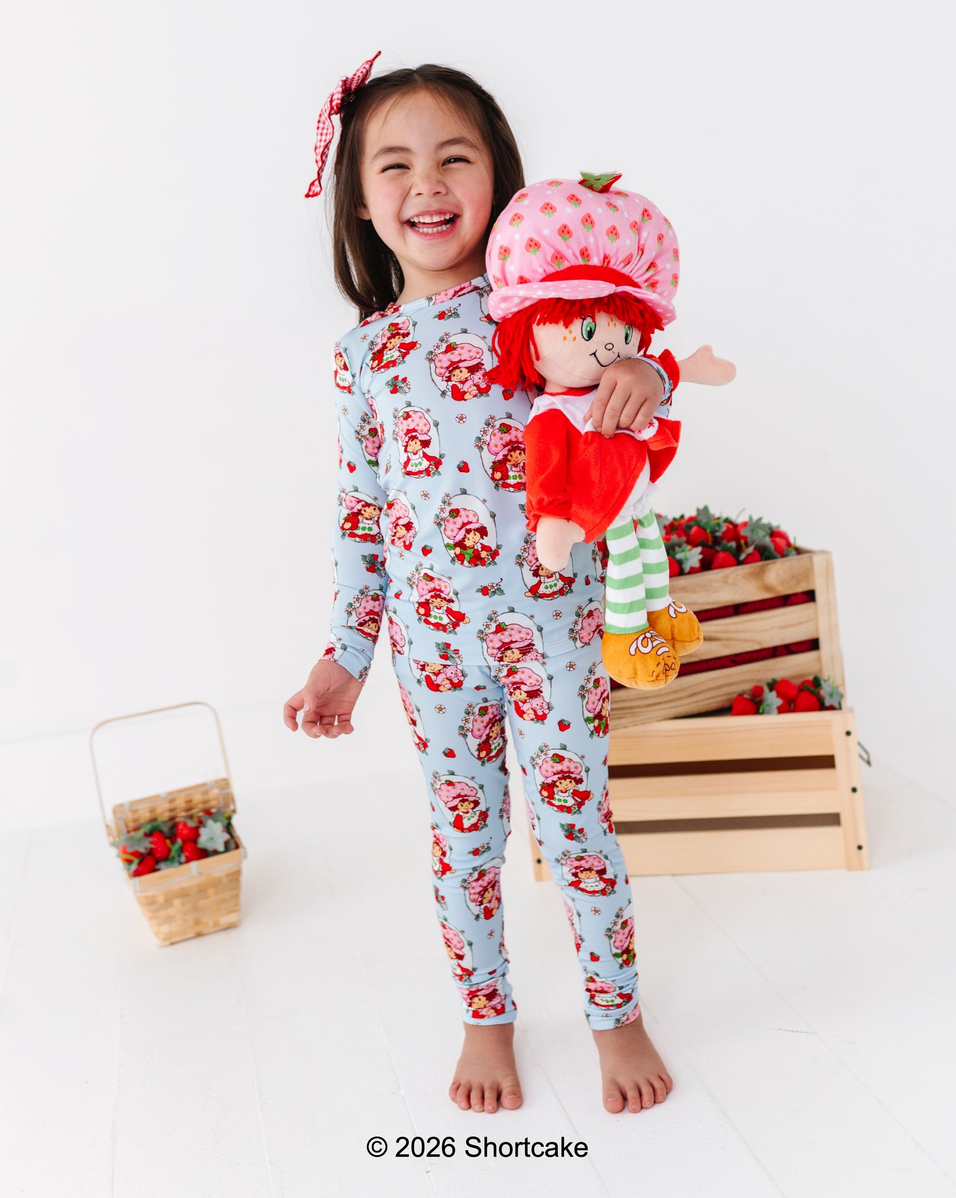 Little girl wearing a Strawberry Shortcake™ bamboo two-piece pajama set and holding a Strawberry Shortcake™ doll