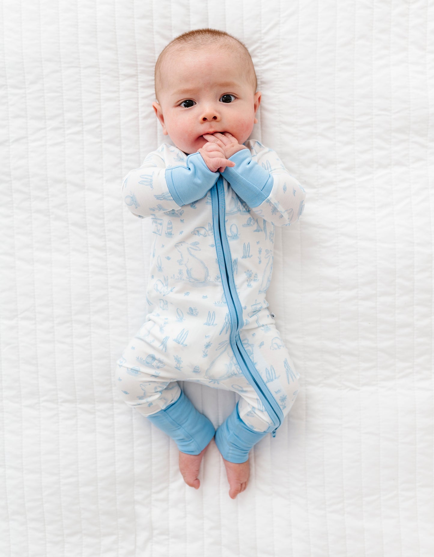 Baby wearing a white and blue Easter bamboo romper on a white textured surface